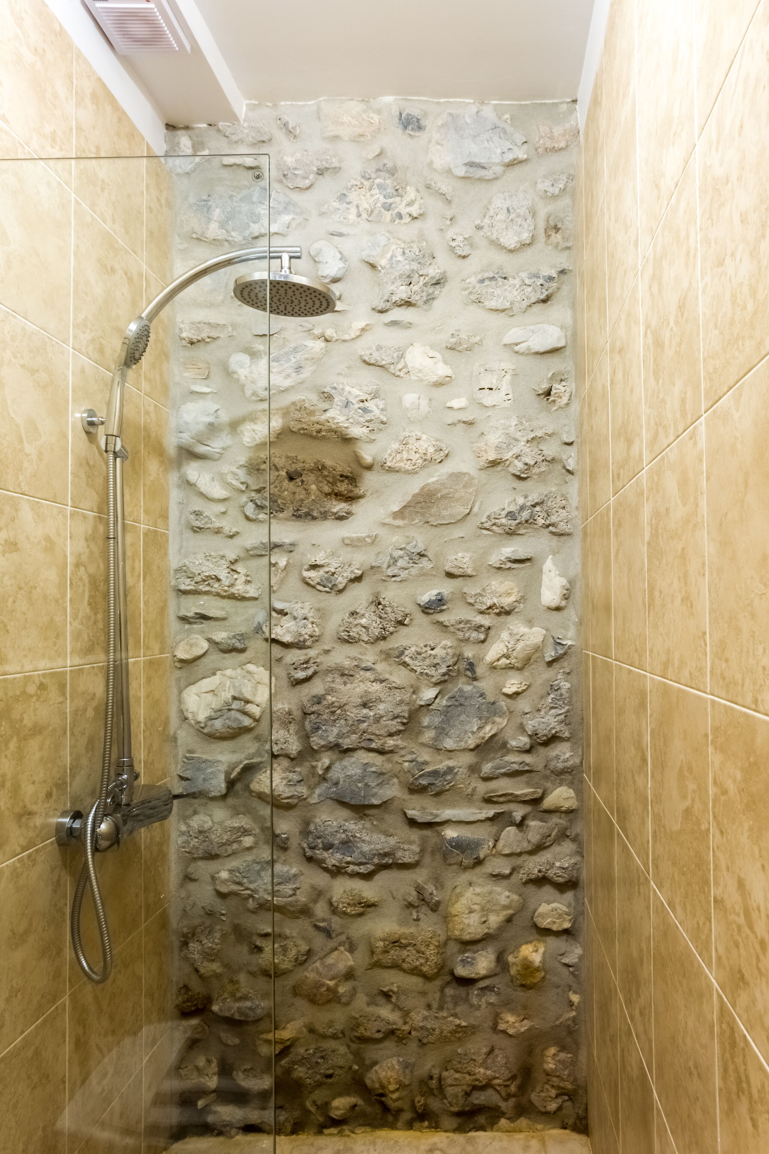 Una ducha con pared de piedra y puerta de cristal.
