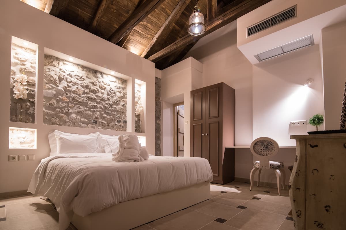 A bedroom with a stone wall, a bed, a wooden wardrobe, and a chair.