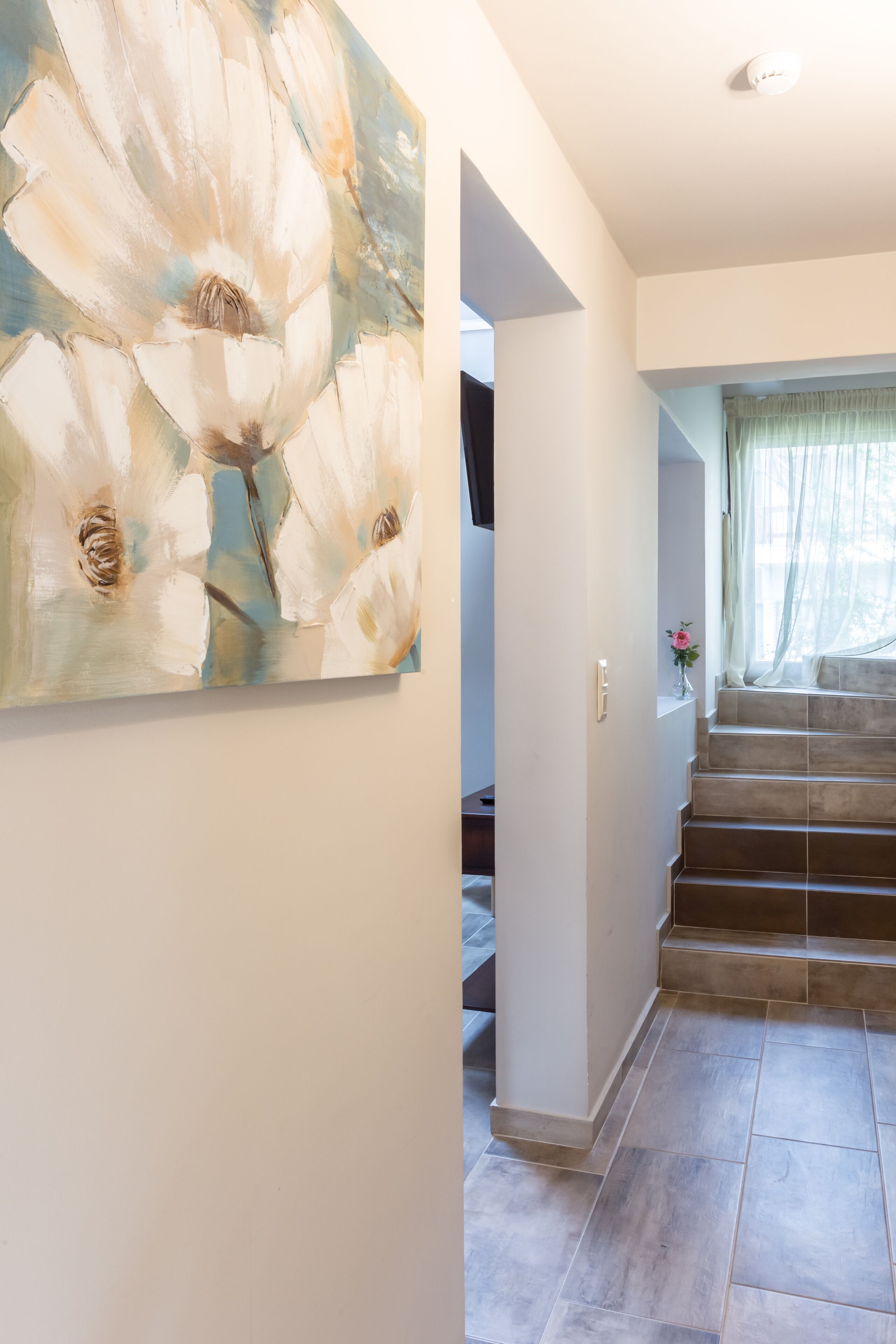A modern interior with a staircase, a large abstract painting on the wall, and a small vase with a flower.