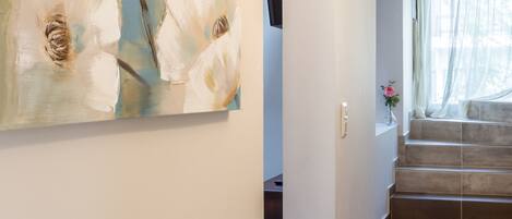 A modern interior with a staircase, a large abstract painting on the wall, and a small vase with a flower.