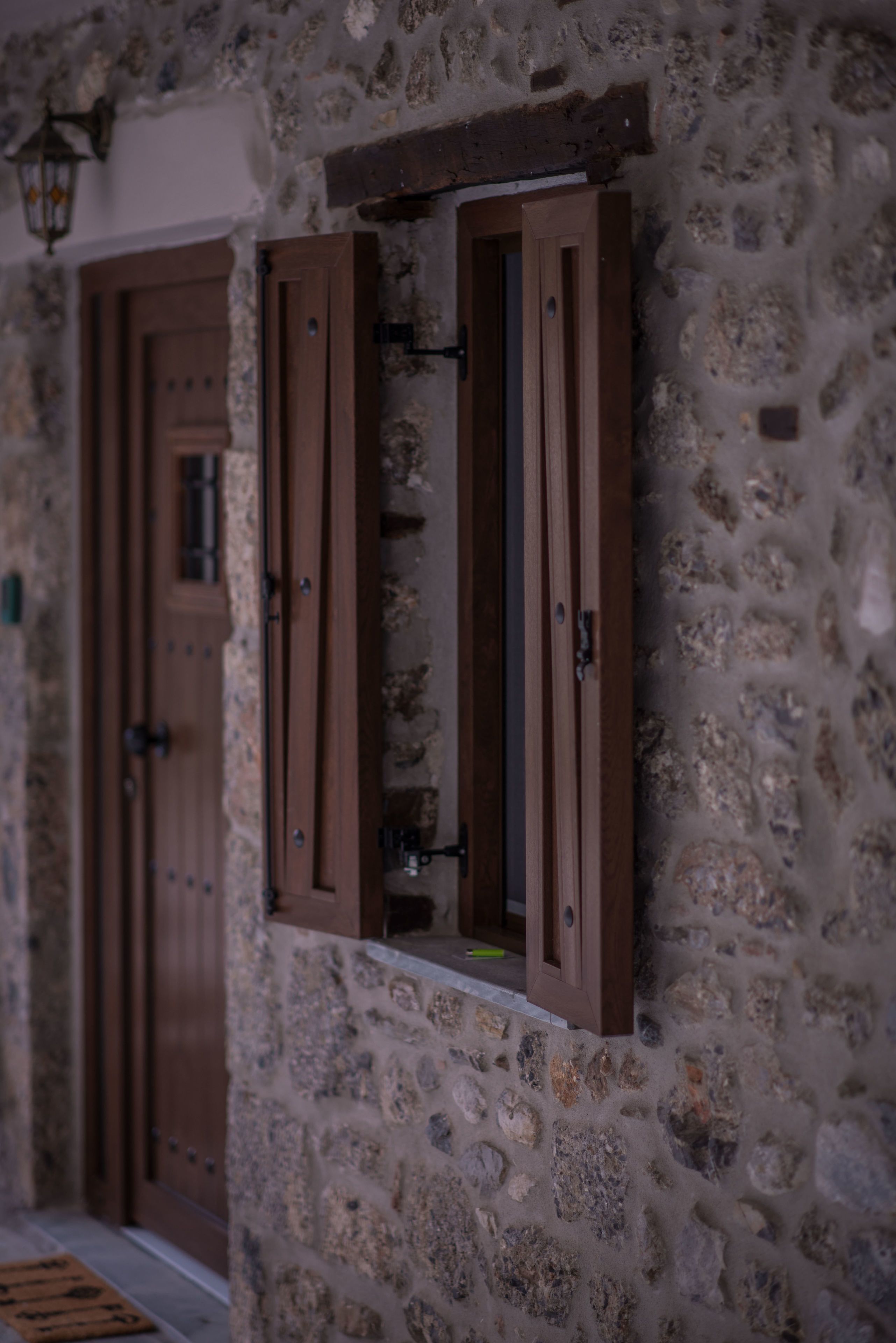 Un muro de piedra con una puerta de madera y una ventana con contraventanas de madera.