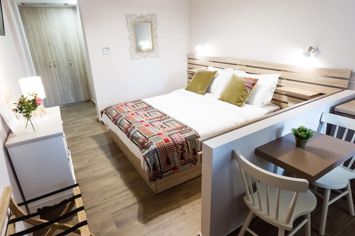 A compact bedroom with a bed, bedside table, chair, and a small table with a plant.