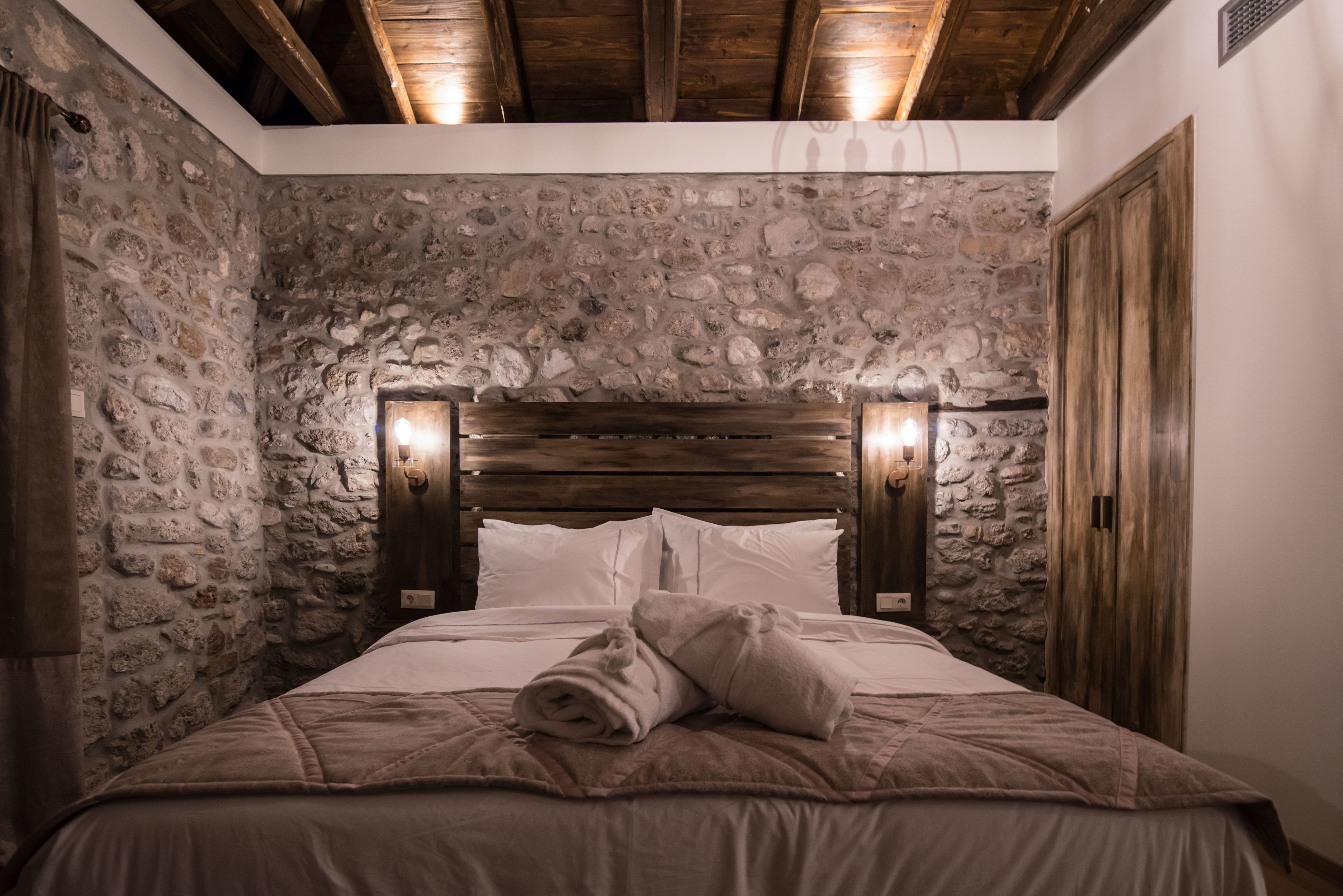 A bedroom with stone walls, a wooden headboard, and a neatly made bed with towels.