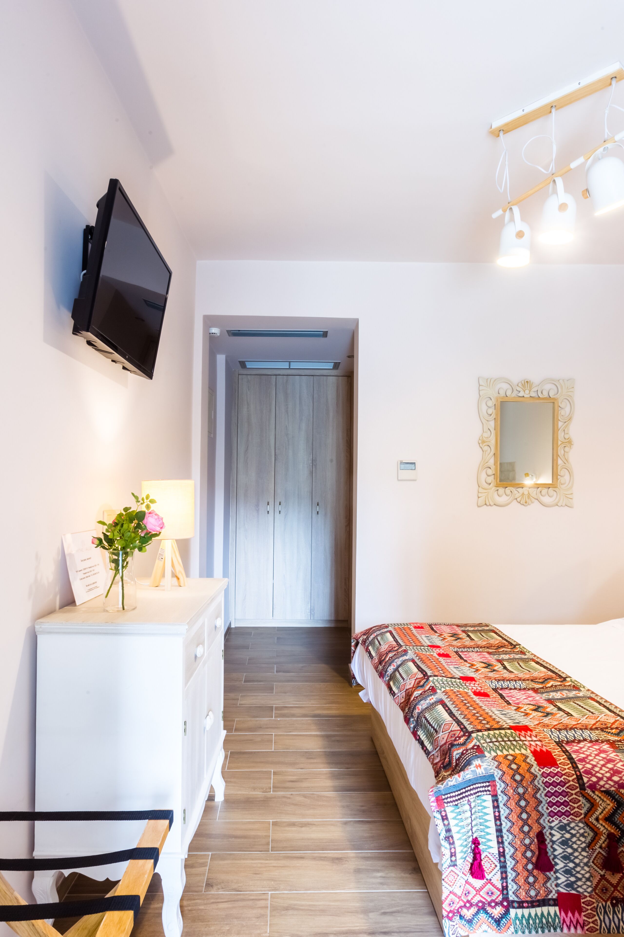 A bedroom with a bed, a dresser, a TV, a mirror, and a hallway leading to a door.