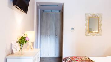 A bedroom with a bed, a dresser, a TV, a mirror, and a hallway leading to a door.