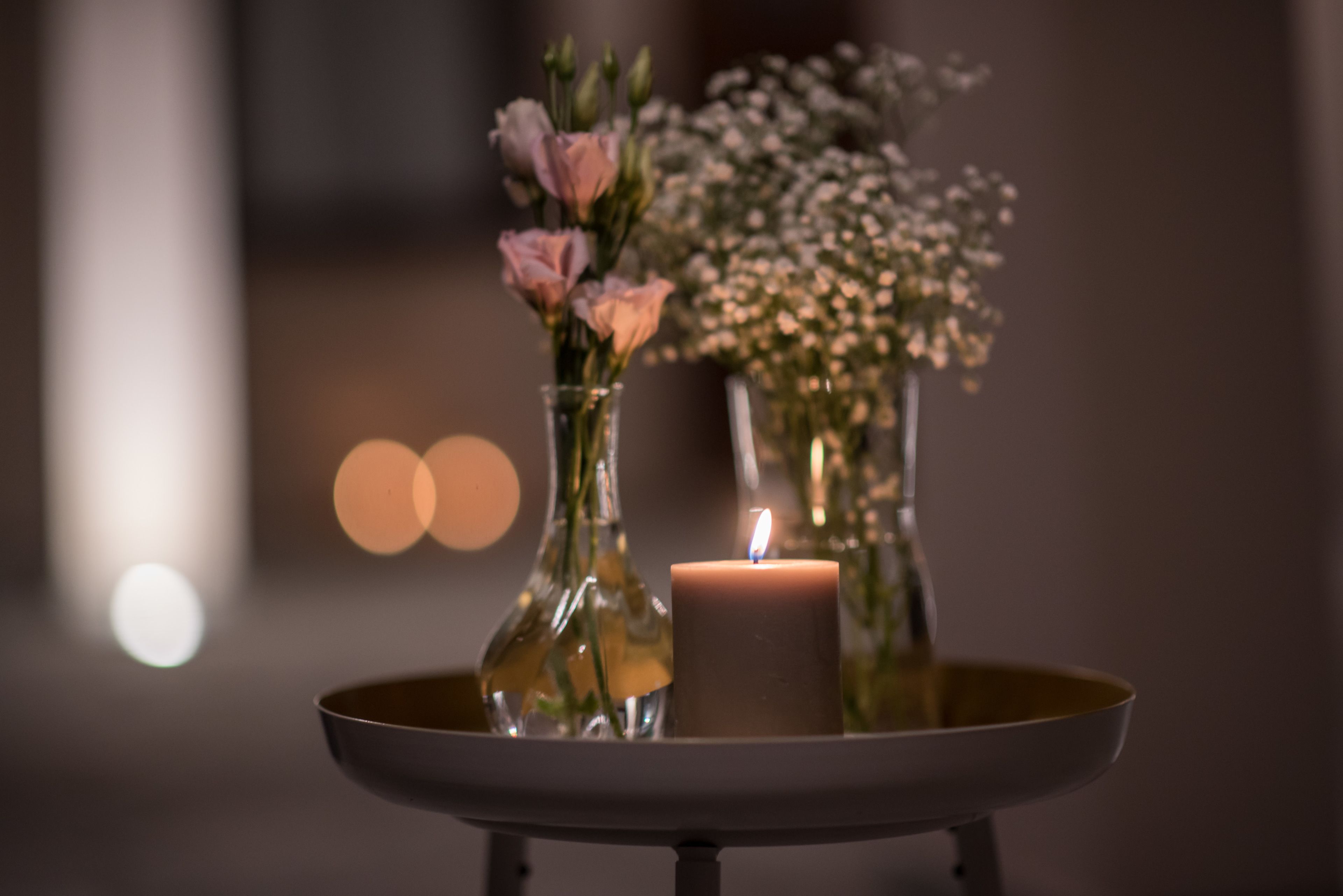 A candle on a tray with two vases of flowers.