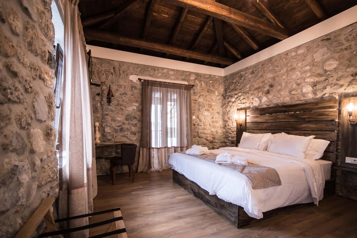 A bedroom with stone walls, a wooden bed, a desk, and a chair.