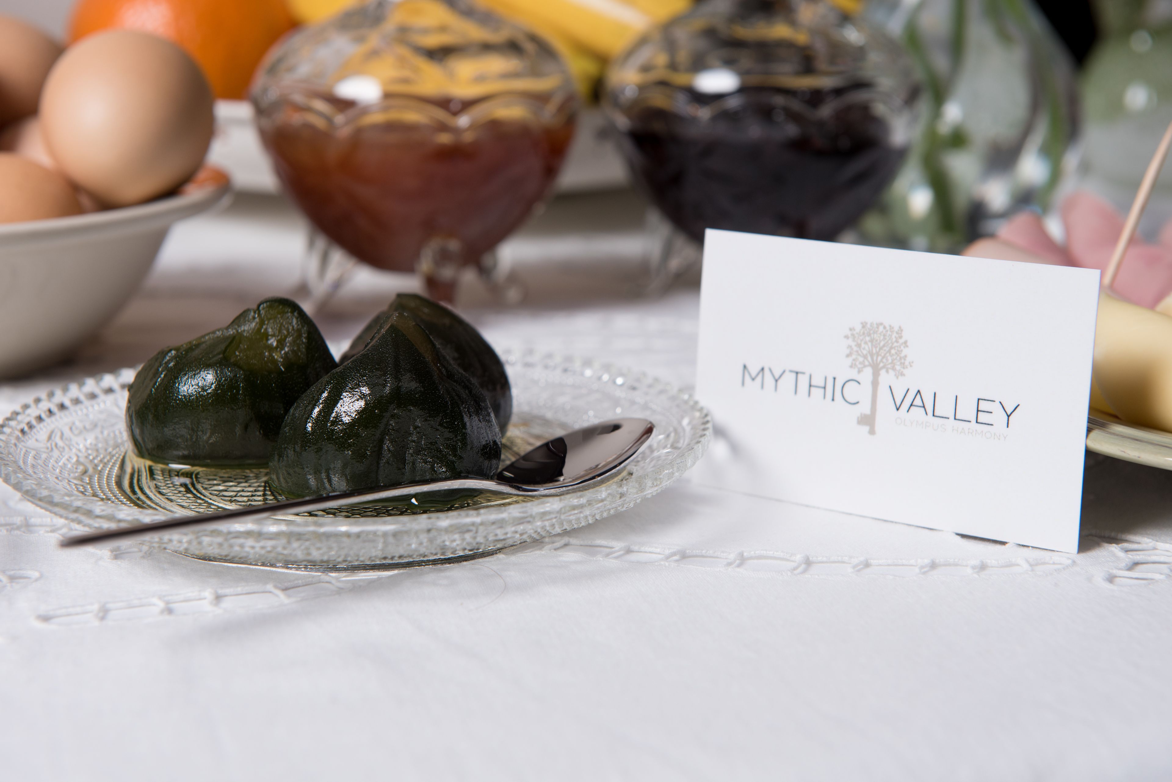 A table with a white placemat, a glass plate with two greenish-brown items, a spoon, and a card labeled "MYTHIC VALLEY."