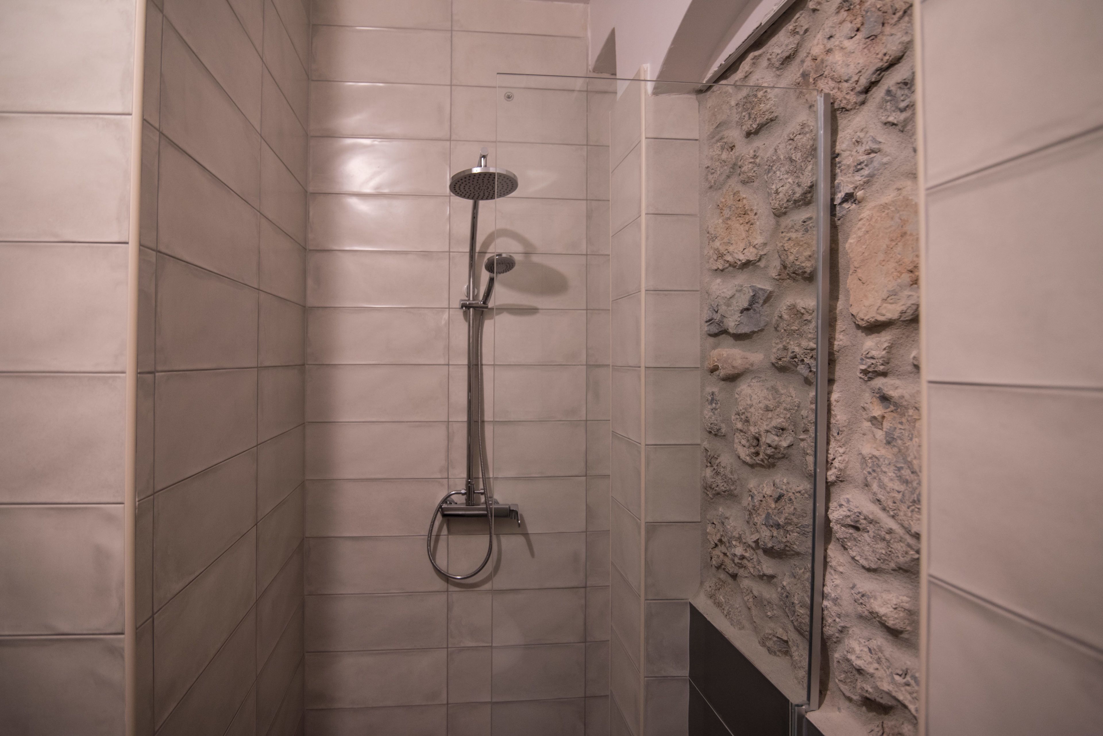 A shower with a stone wall and tiled floor.
