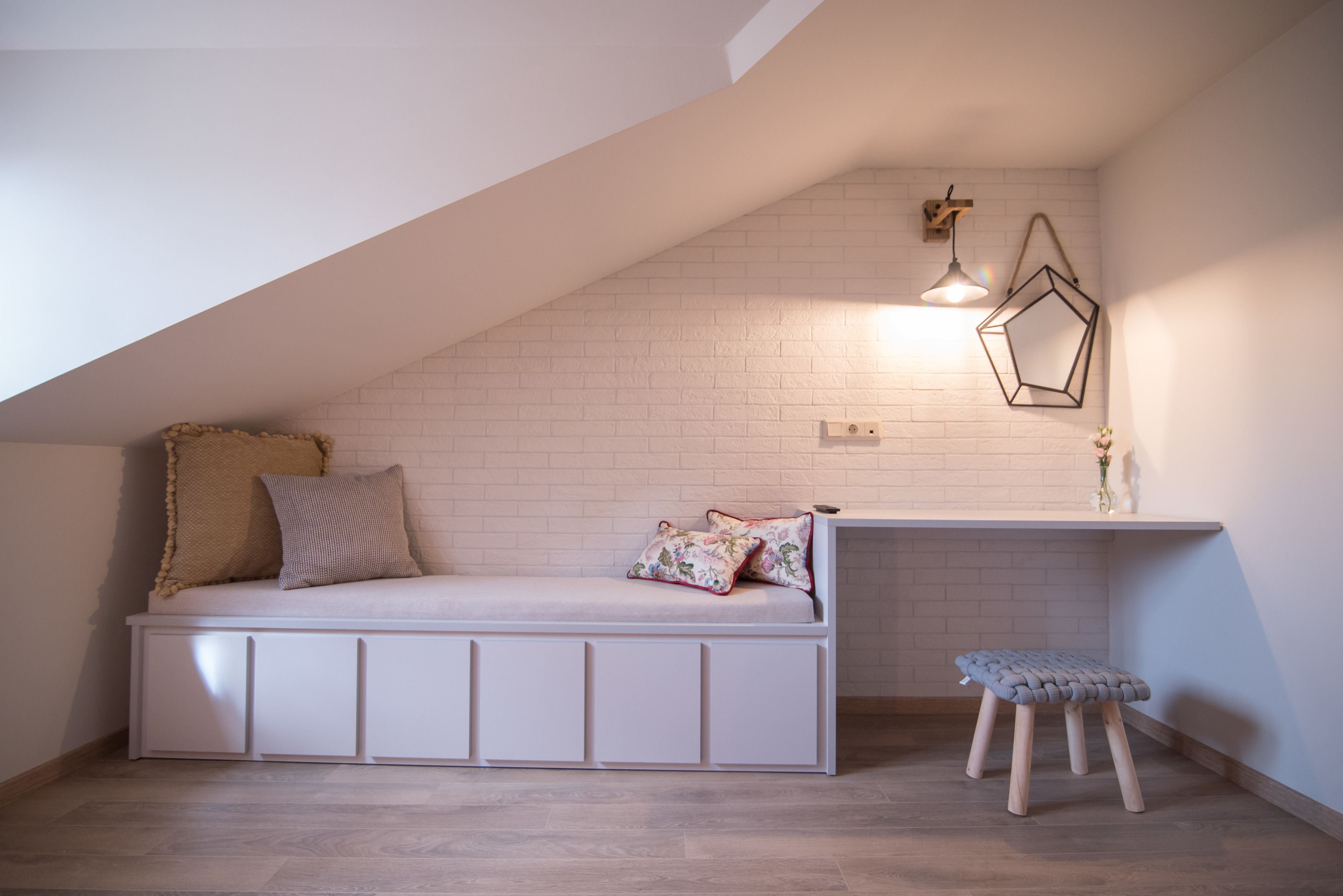 Ein gemütliches Schlafzimmer im Dachgeschoss mit eingebauter Bank, einem kleinen Hocker und einer geneigten Decke.