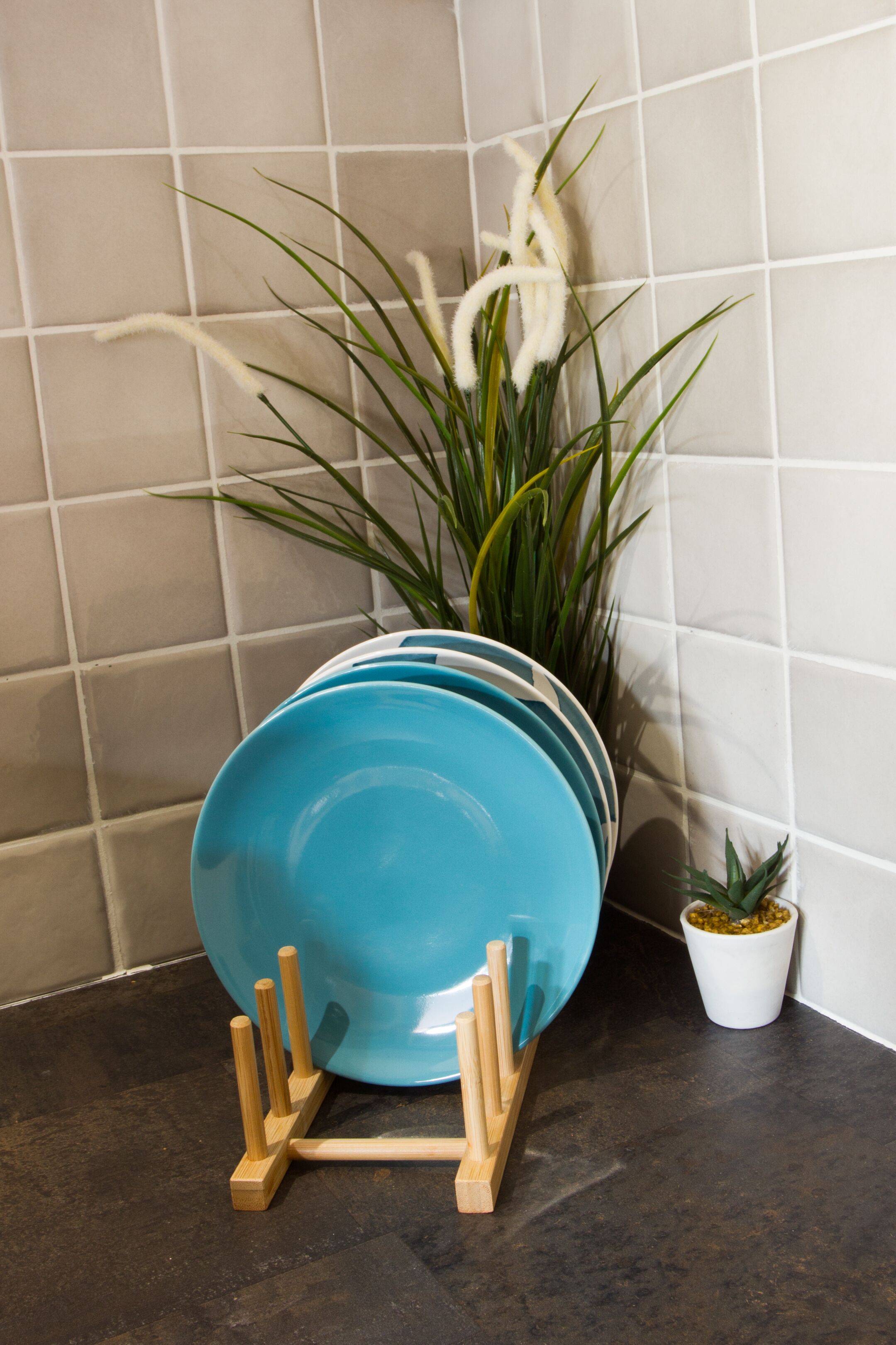 Un comptoir de cuisine sur lequel se trouve un égouttoir bleu contenant plusieurs assiettes, une plante en pot et un petit pot blanc avec une plante.