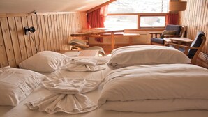 Une chambre confortable, aménagée dans le style d’un chalet, avec un intérieur en bois, un lit avec du linge de maison blanc, un bureau et une chaise.