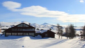 Un grand bâtiment en bois à deux étages, doté d’un toit en pente, entouré d’un paysage enneigé et avec des montagnes en arrière-plan.