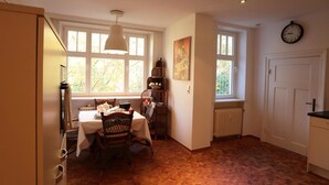 Un comedor con una mesa dispuesta para cuatro, una silla de mimbre, una lámpara colgante y una ventana con vistas a árboles.