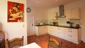 Una cocina moderna con armarios blancos, encimera negra y comedor con sillas de mimbre.