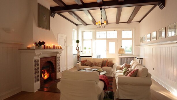 Una sala de estar acogedora con chimenea, muebles blancos y un techo alto con vigas a la vista.