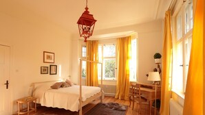 Un dormitorio con una cama con dosel, un escritorio con silla, una lámpara y una ventana con cortinas.