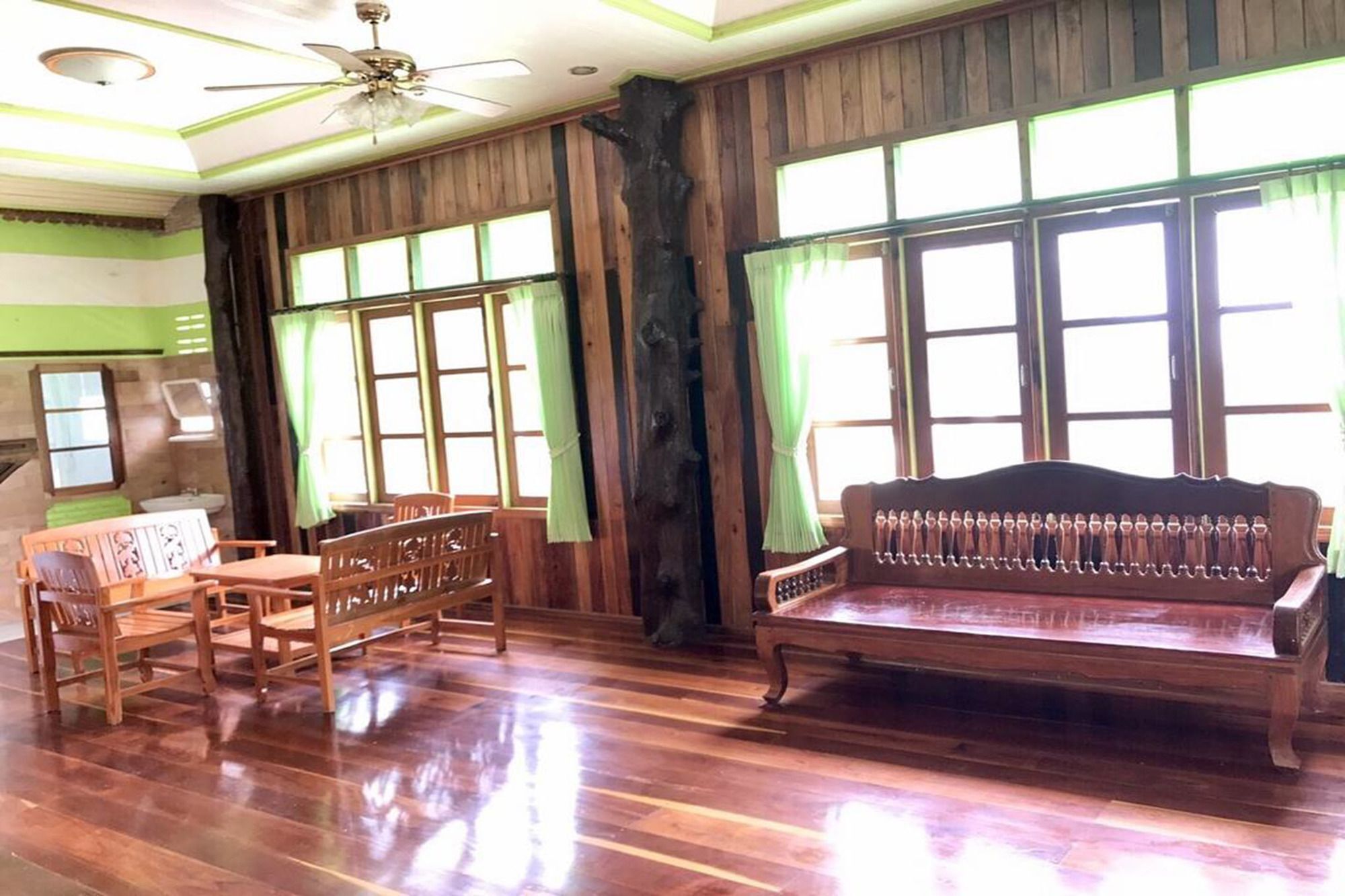 A room with wooden flooring, a ceiling fan, a wooden bench, a table with chairs, and large windows with curtains.