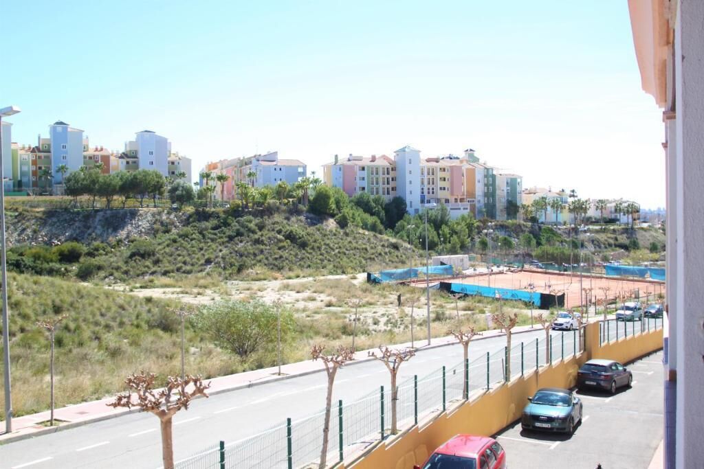 A residential area with multi-story buildings, a road with parked cars, and sparse vegetation.