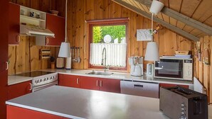 A compact kitchen with wooden walls, a large window, and basic appliances including a stove, microwave, and toaster. - Juwel Feriendorf - Bockholm Haus 19 (Gluecksburg)