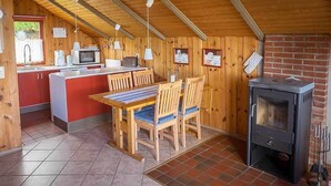 A cozy kitchen with wooden walls, a tiled floor, a dining table with chairs, a stove, and a window with a view of greenery. - Juwel Feriendorf - Bockholm Haus 19 (Gluecksburg)