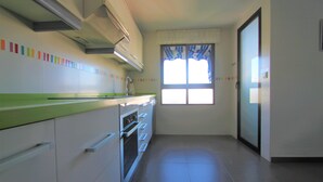 A kitchen with white cabinets, a green countertop, and a window with a striped curtain. - Apartamento CasaTuris Portobello (Alicante)