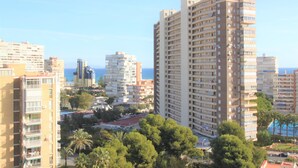 A high-rise building with multiple balconies, surrounded by other buildings and palm trees, overlooking a coastal area. - Apartamento CasaTuris Portobello (Alicante)
