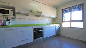 A kitchen with white cabinets, a microwave, an oven, and a green countertop. - Apartamento CasaTuris Portobello (Alicante)