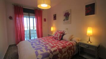 Un dormitorio con cama, dos lámparas de noche, una mesita de noche, una ventana con cortinas y un cuadro en la pared.