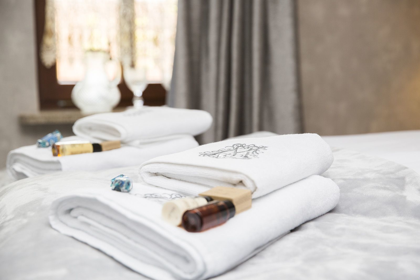 Un conjunto ordenado de toallas blancas con un logotipo, sobre una cama con cubierta texturizada.