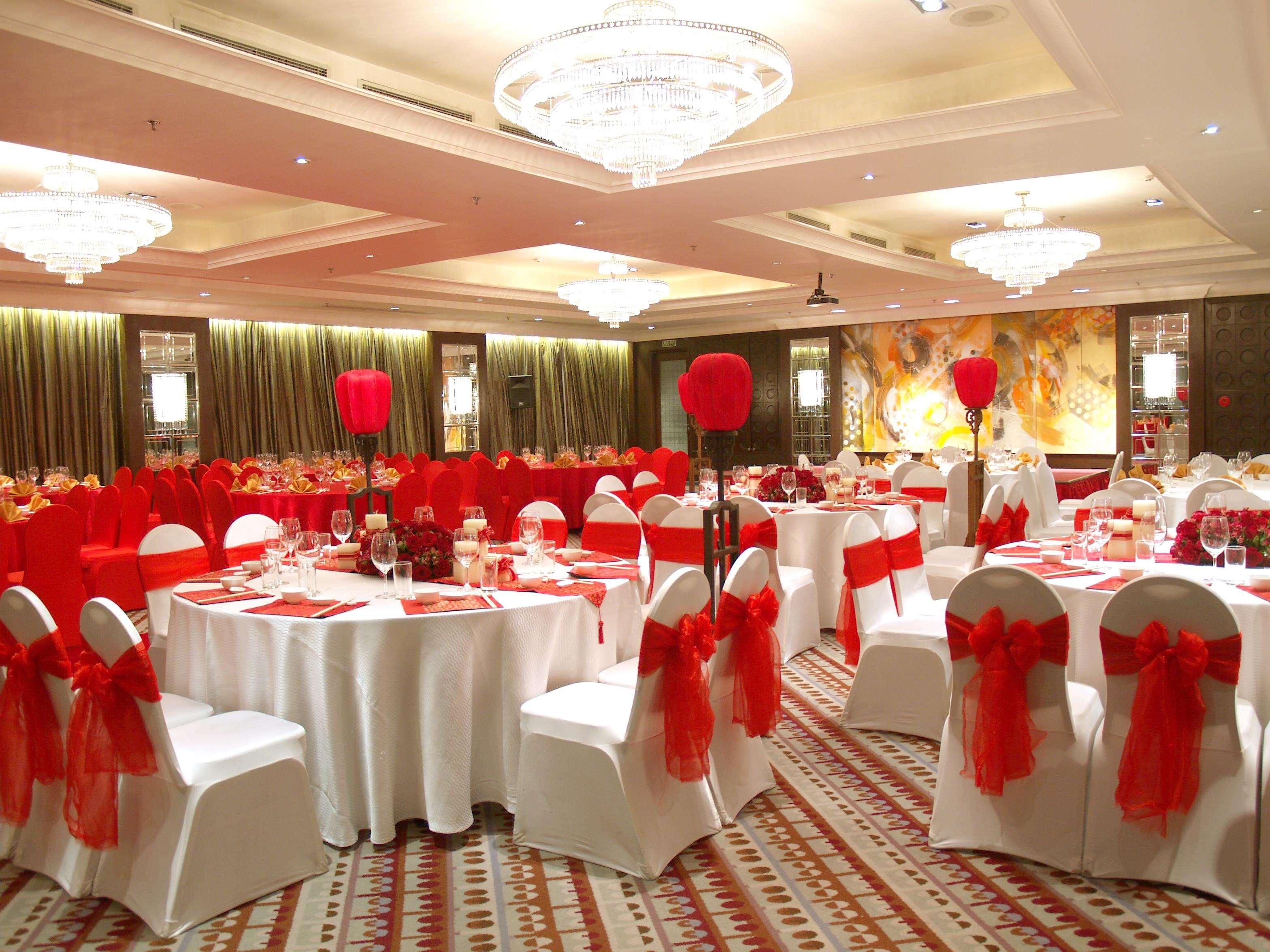 A banquet hall with round tables, red and white chairs, and chandeliers.