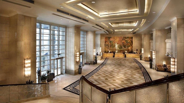 Um hall espaçoso com teto alto, grandes janelas, um balcão de recepção central e piso estampado.