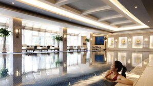 Uma piscina interior ampla, com água cristalina, áreas iluminadas pelo sol e assentos ao longo das laterais.