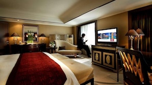 Quarto de hotel com uma cama grande, televisão, área de estar e escrivaninha.