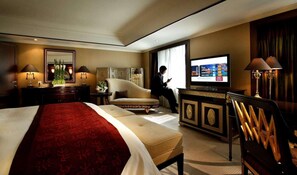 Una habitación de hotel con una cama grande, televisión, zona de estar y escritorio.