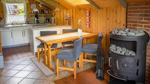 A cozy cabin with a wooden interior, a dining area with a table and chairs, a kitchen with modern appliances, and a wood stove. - Juwel Feriendorf Glücksburg - Holnis 13 (Gluecksburg)