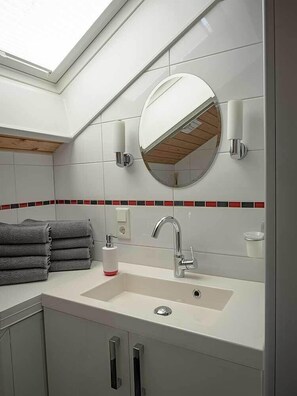 A modern bathroom with a skylight, a round mirror, a white sink, and a towel rack.