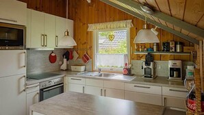 A compact kitchen with white cabinets, a stove, a sink, and a coffee maker. - Juwel Feriendorf Glücksburg - Holnis 13 (Gluecksburg)