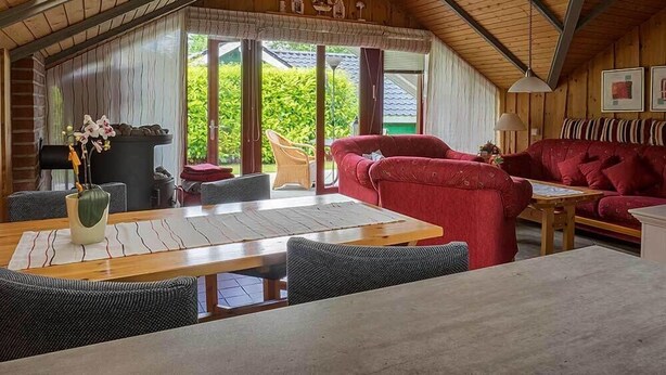 A cozy cabin interior with a dining area, red sofa, and a view of greenery outside. - Juwel Feriendorf Glücksburg - Holnis 13 (Gluecksburg)
