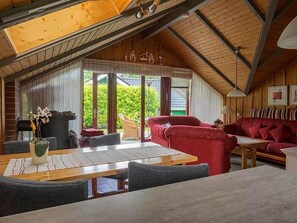 A cozy cabin interior with a dining area, red sofa, and a view of greenery outside.