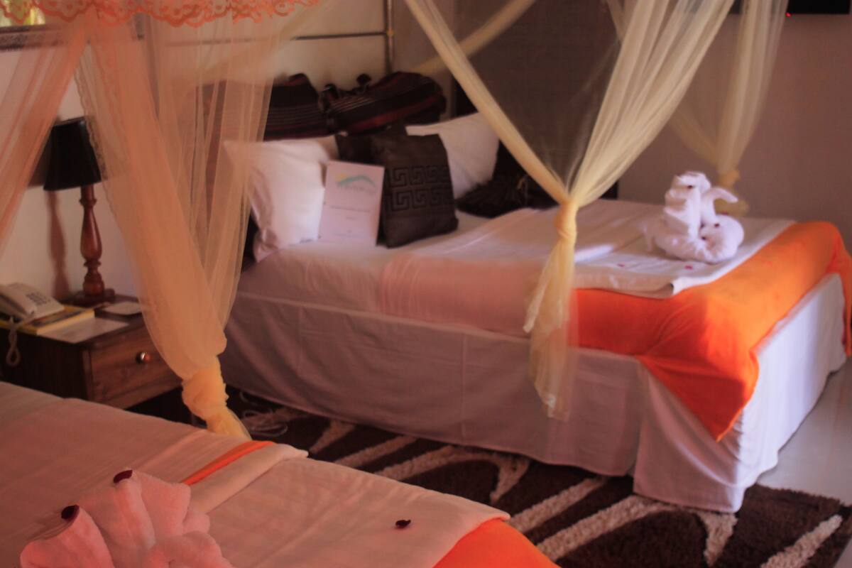 Quarto de hotel com duas camas, uma mesinha de cabeceira e uma mala.