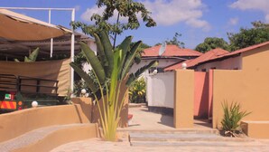 Une cour avec un sol carrelé, une grande plante et un véhicule garé au fond.
