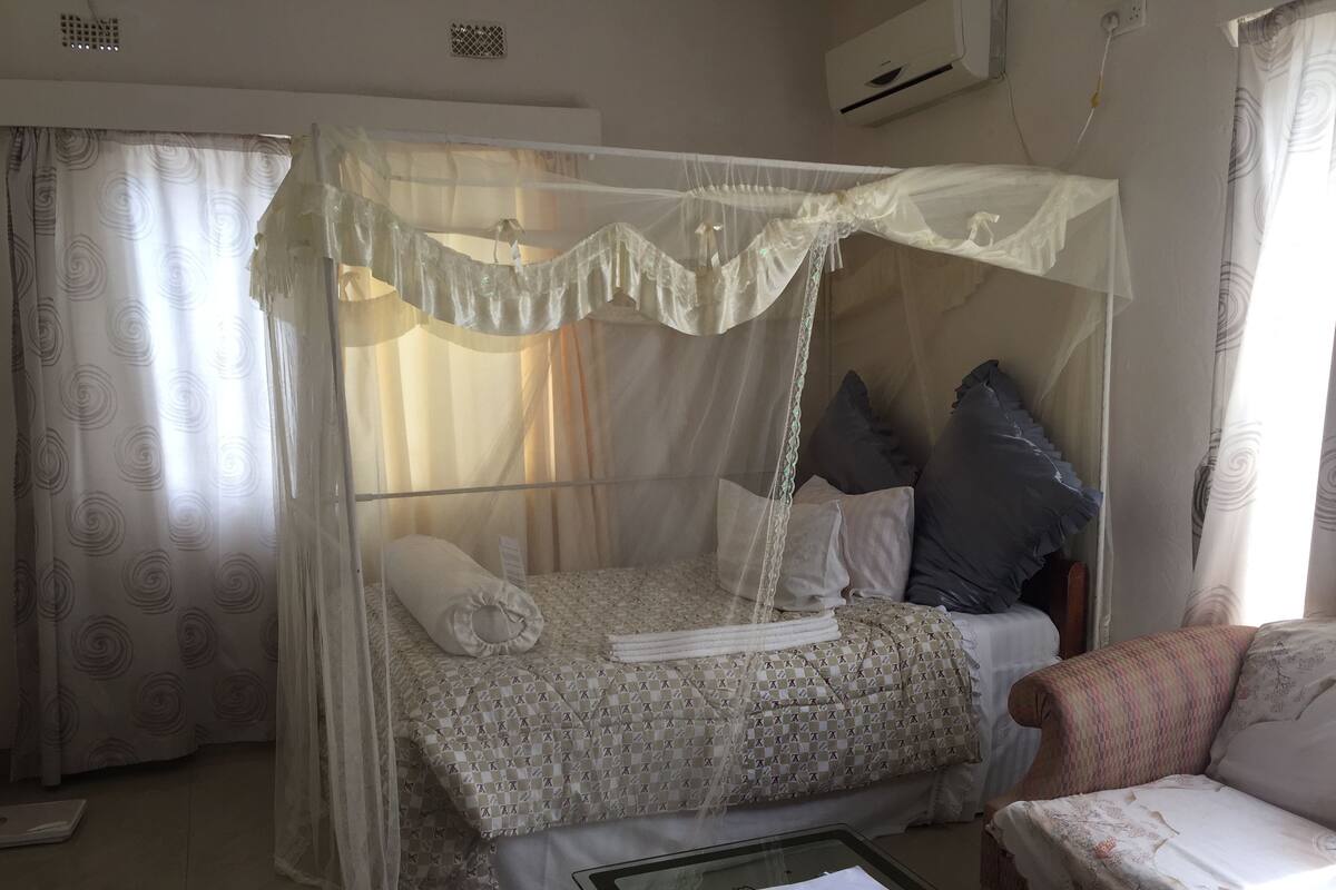 Quarto com cama de dossel, um sofá, mesa de centro de vidro e cama com colcha estampada.