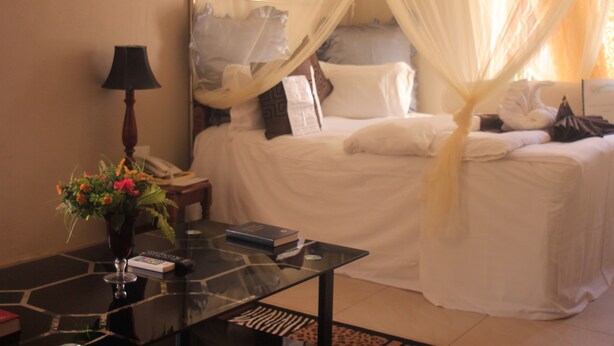 Une chambre d’hôtel avec un lit, une table basse en verre, une lampe et un vase rempli de fleurs.