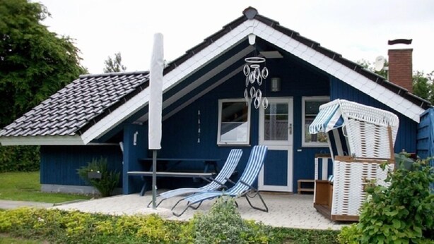 A blue house with a tiled roof, a covered seating area with two lounge chairs, and a small garden. - Juwel Feriendorf - Lille Blå Søster (Gluecksburg)