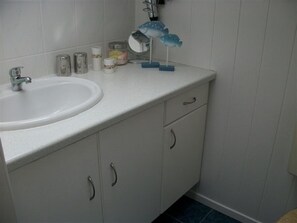 Un bany amb un lavabo blanc, un mirall i alguns productes de tocador sobre la superfície.
