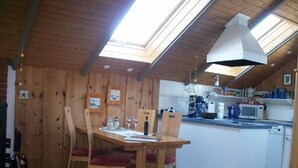 A cozy kitchen with wooden walls, a dining table with chairs, and a skylight above. - Juwel Feriendorf - Lille Blå Søster (Gluecksburg)
