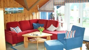 A cozy room with a red sofa, blue armchair, and a wooden coffee table. - Juwel Feriendorf - Lille Blå Søster (Gluecksburg)