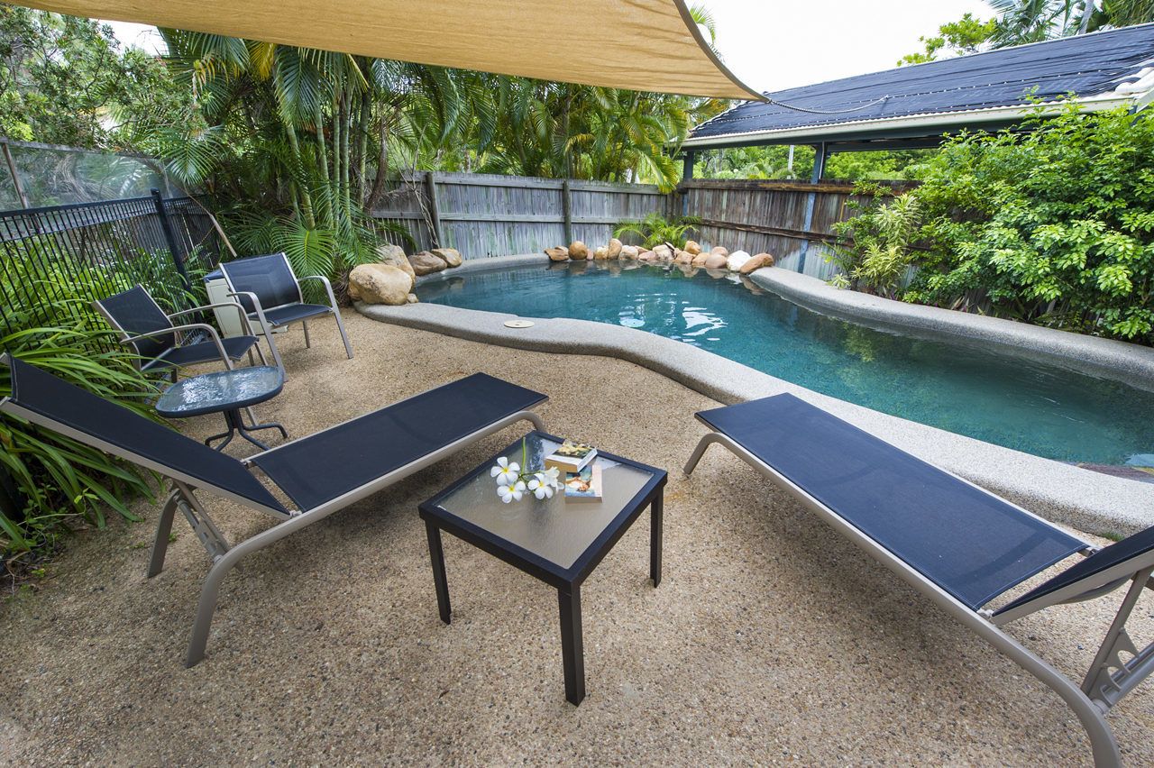 A pool area with lounge chairs, a table, and a wooden fence.