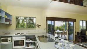 A compact kitchen with a built-in oven, microwave, and sink. A dining area with a table and chairs is visible through a sliding glass door. - Manyana (Nelly Bay)